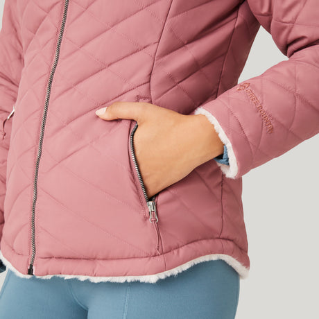 A person wears the Clearance Women's FreeCycle® Cloud Lite II Reversible Jacket in pink with a zippered pocket and white fleece trim, their hand in the pocket. They are also wearing blue leggings.