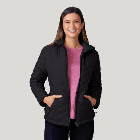A woman smiles at the camera with hands in pockets, wearing the Clearance Women's FreeCycle® Cloud Lite II Reversible Jacket over a pink shirt, standing against a light gray background.