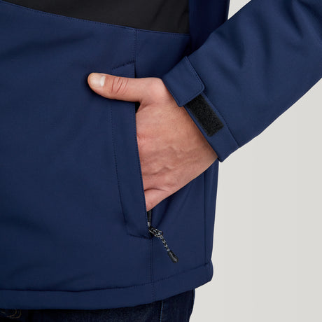 A person is shown from the waist down, wearing the Clearance Men's Thermo Softshell® Mid Weight Jacket in blue with a black panel. The jacket has a zippered pocket and Velcro strap on the sleeve. Background is plain and light-colored.