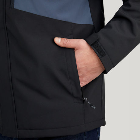 A person wears the Clearance Men's Thermo Softshell® Mid Weight Jacket—black with a blue section, visible zipper, Velcro strap on the sleeve, and their right hand in the pocket.