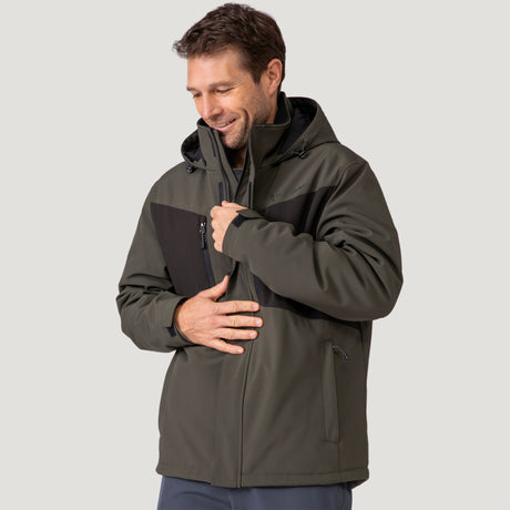 A man wearing the Clearance Men's Thermo Softshell® Mid Weight Jacket in green and black smiles while zipping it up. He looks relaxed and is gazing slightly downward against a plain light gray background.