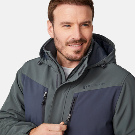 [Joe is 6'0" wearing size M.] Men’s Free Country two-tone hooded zip-front jacket with dark gray body and black paneling across shoulders and chest—features dual vertical zippered chest pockets, side hand pockets, full-length front zipper, and an attached interior snow skirt for enhanced protection against the elements. Paired with matching gray pants for a sleek, coordinated winter look.