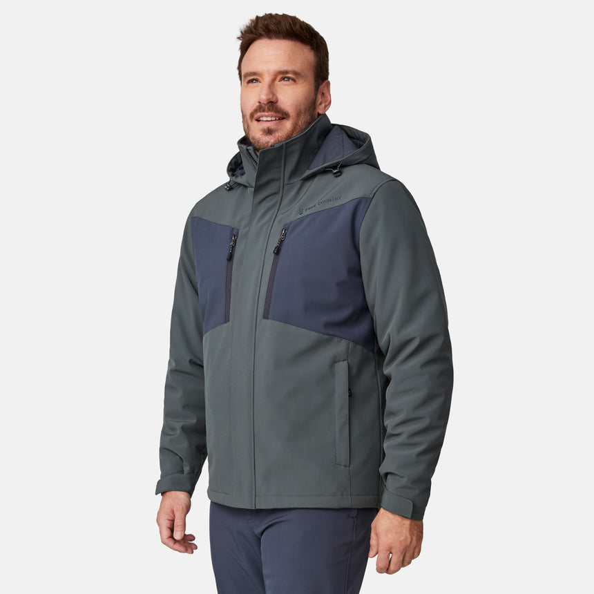 [Joe is 6'0" wearing size M.] Men’s Free Country two-tone hooded zip-front jacket with dark gray body and black paneling across shoulders and chest—features dual vertical zippered chest pockets, side hand pockets, full-length front zipper, and an attached interior snow skirt for enhanced protection against the elements. Paired with matching gray pants for a sleek, coordinated winter look.
