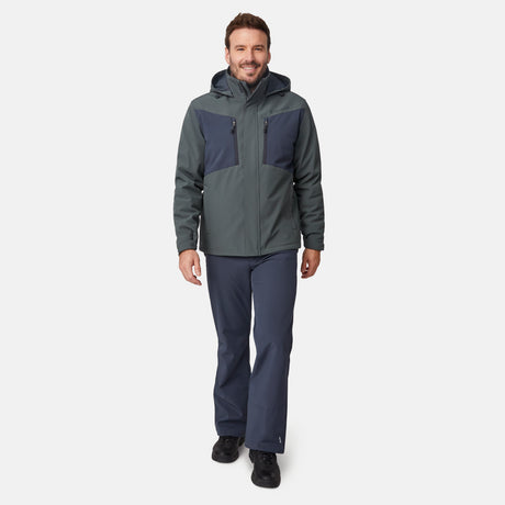 A smiling man wearing a grey and navy Free Country Men’s Thermo Softshell® Mid Weight Jacket, featuring a water-resistant, three-layer bonded fabric hood, paired with matching trousers and black boots.