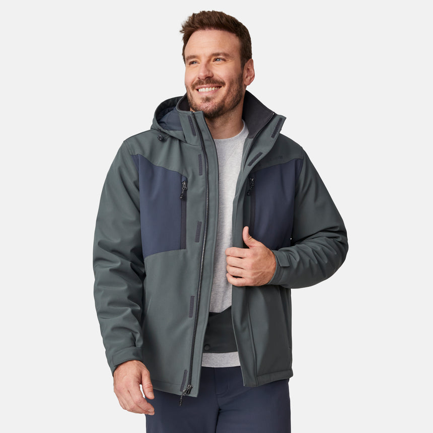 [Joe is 6'0" wearing size M.] Men’s Free Country two-tone hooded zip-front jacket with dark gray body and black paneling across shoulders and chest—features dual vertical zippered chest pockets, side hand pockets, full-length front zipper, and an attached interior snow skirt for enhanced protection against the elements. Paired with matching gray pants for a sleek, coordinated winter look.
