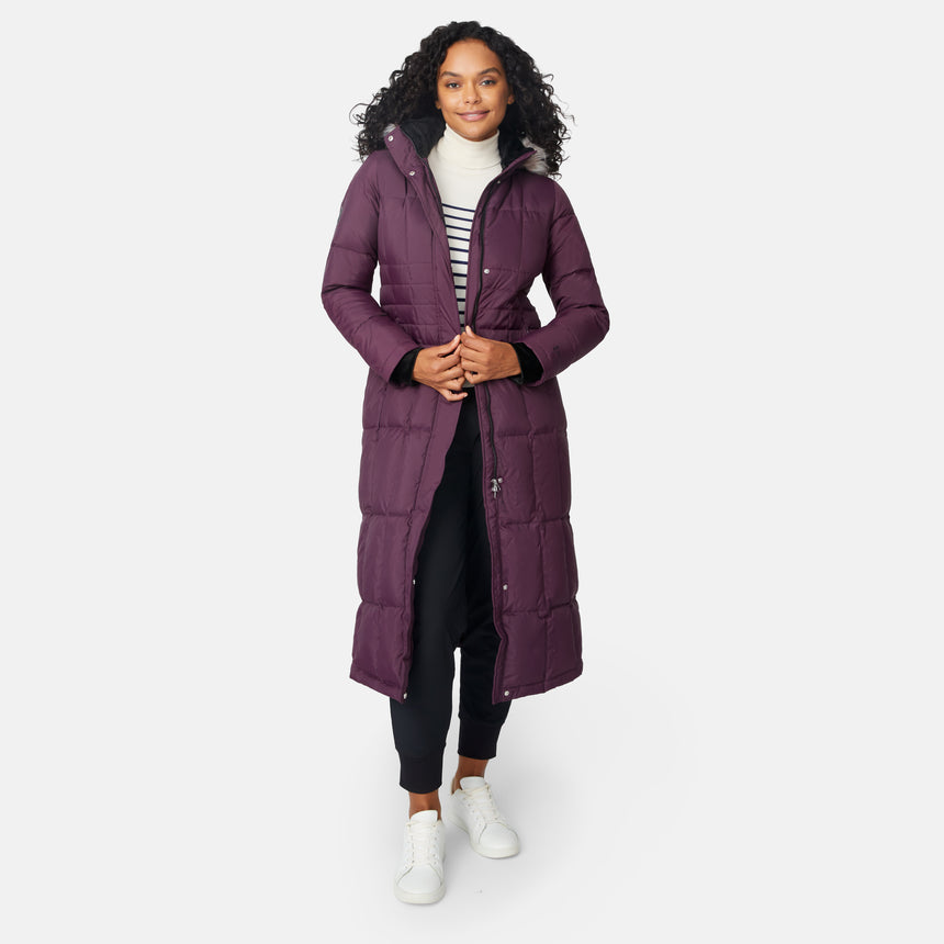 [Angelique is 5'10" wearing size S.] Woman wearing Free Country Women's Full Length Splendor Down Jacket in burgundy with a full front zipper opening, lower pockets, calf length, a detachable hood with faux fur trim, and water resistant and wind resistant stretch performance fabric, light grey background. Best women’s jacket for winter weather.