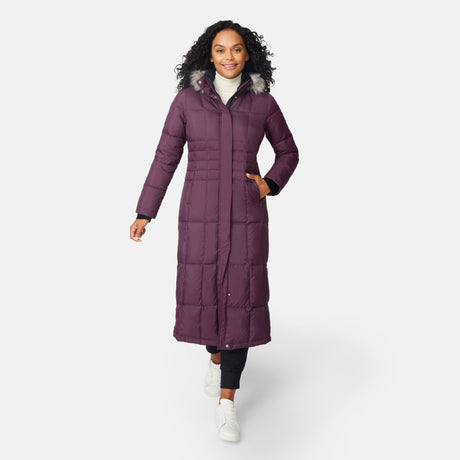 [Angelique is 5'10" wearing size S.] Woman wearing Free Country Women's Full Length Splendor Down Jacket in burgundy with a full front zipper opening, lower pockets, calf length, a detachable hood with faux fur trim, and water resistant and wind resistant stretch performance fabric, light grey background. Best women’s jacket for winter weather.