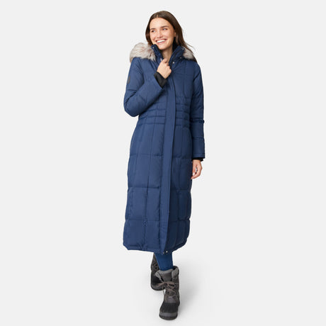 [Jessica is 5'9.5" wearing size S.] Woman wearing Free Country Women's Full Length Splendor Down Jacket in navy blue with a full front zipper opening, lower pockets, calf length, a detachable hood with faux fur trim, and water resistant and wind resistant stretch performance fabric, light grey background. Best women’s jacket for winter weather.