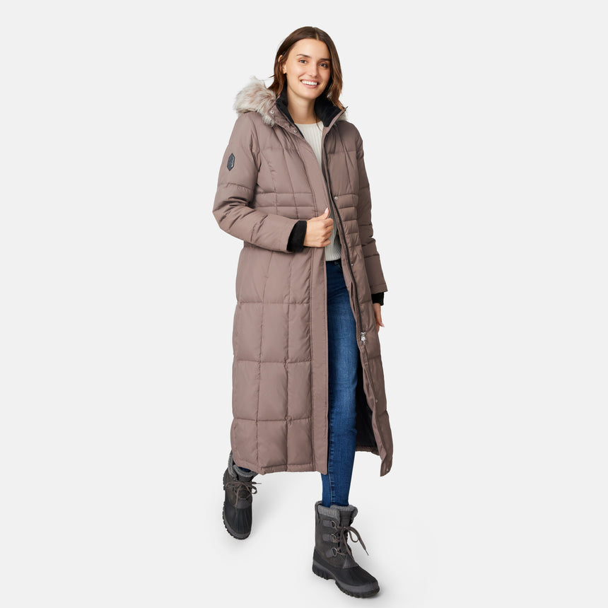 [Jessica is 5'9.5" wearing size S.] Woman wearing Free Country Women's Full Length Splendor Down Jacket in tan with a full front zipper opening, lower pockets, calf length, a detachable hood with faux fur trim, and water resistant and wind resistant stretch performance fabric, light grey background. Best women’s jacket for winter weather.