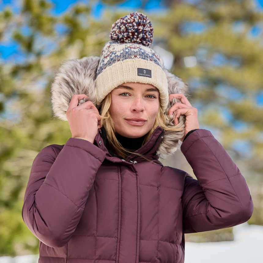 Close up of a woman wearing a burgundy down jacket with a fur trimmed hood outdoors