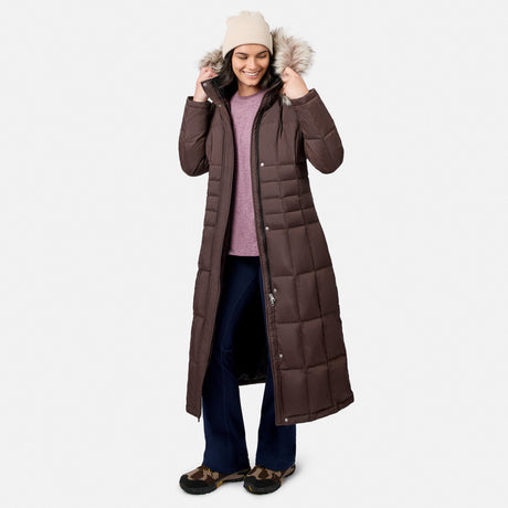 [Model is wearing size S.] A woman modeling a long brown quilted parka with a faux-fur trimmed hood, worn over a mauve sweater and navy pants, on a light gray studio background.