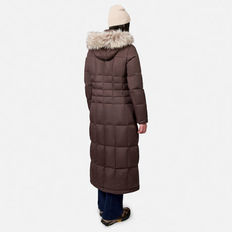 [Model is wearing size S.] A person shown from the back wearing a long brown puffer coat with a faux-fur trimmed hood, a cream beanie, dark blue pants, and brown shoes, against a light gray studio background. 