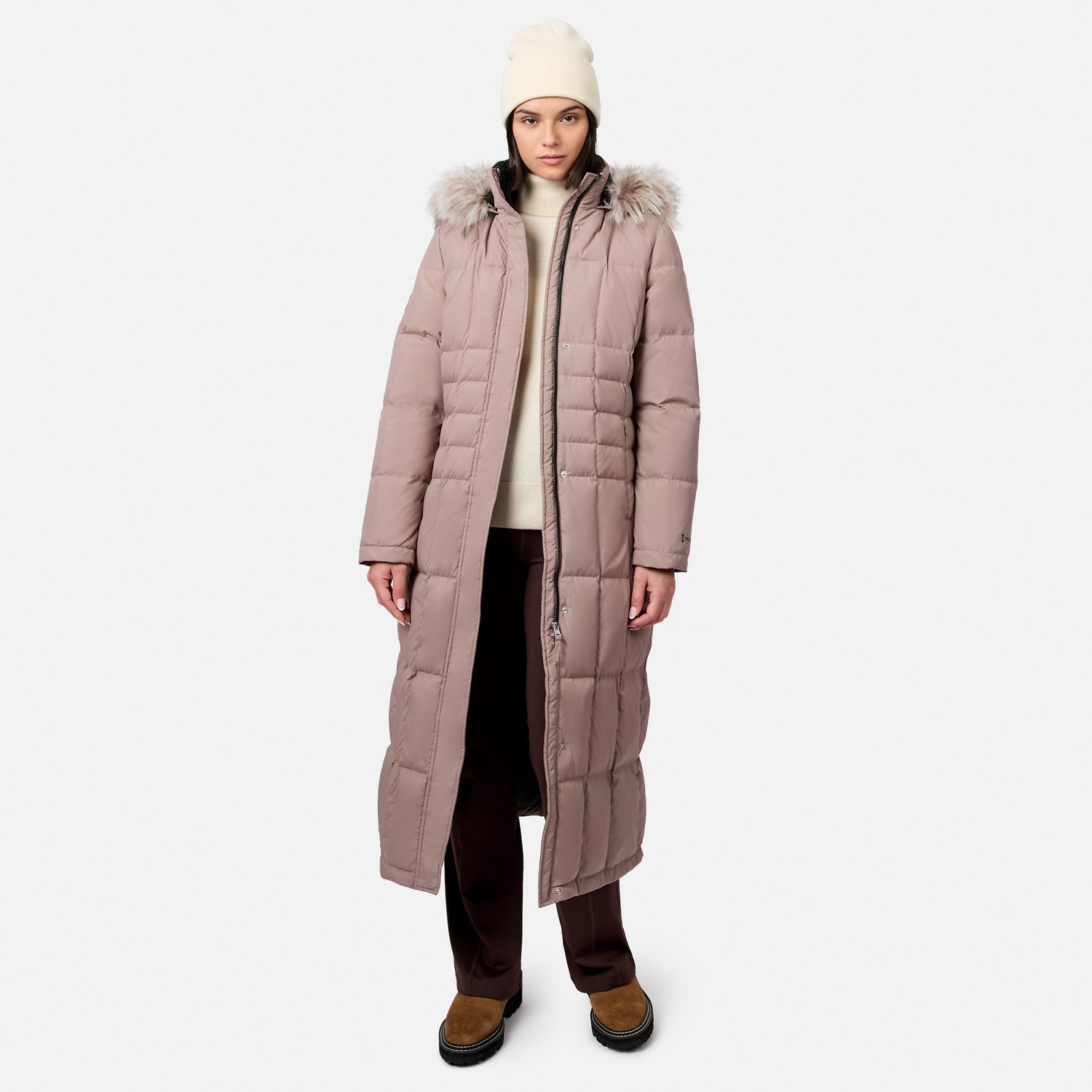 Front view of a model wearing a dusty pink full length Splendor Down Jacket with a fur trimmed hood and a cream knit hat.