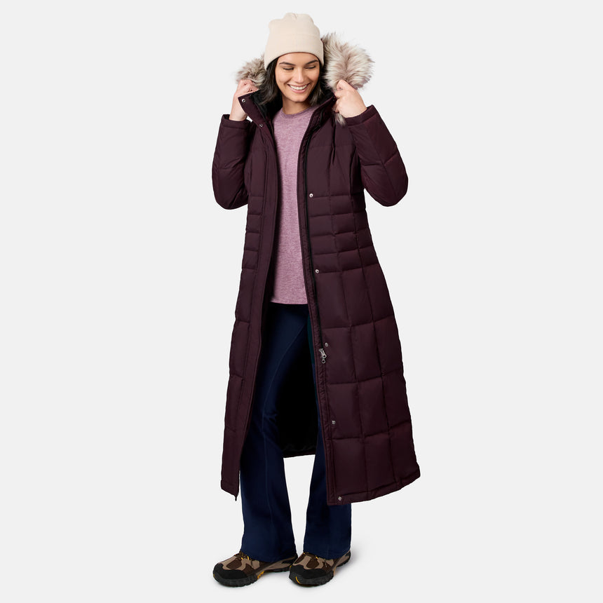 Full body shot of a woman in a burgundy down jacket with a fur hood in a studio