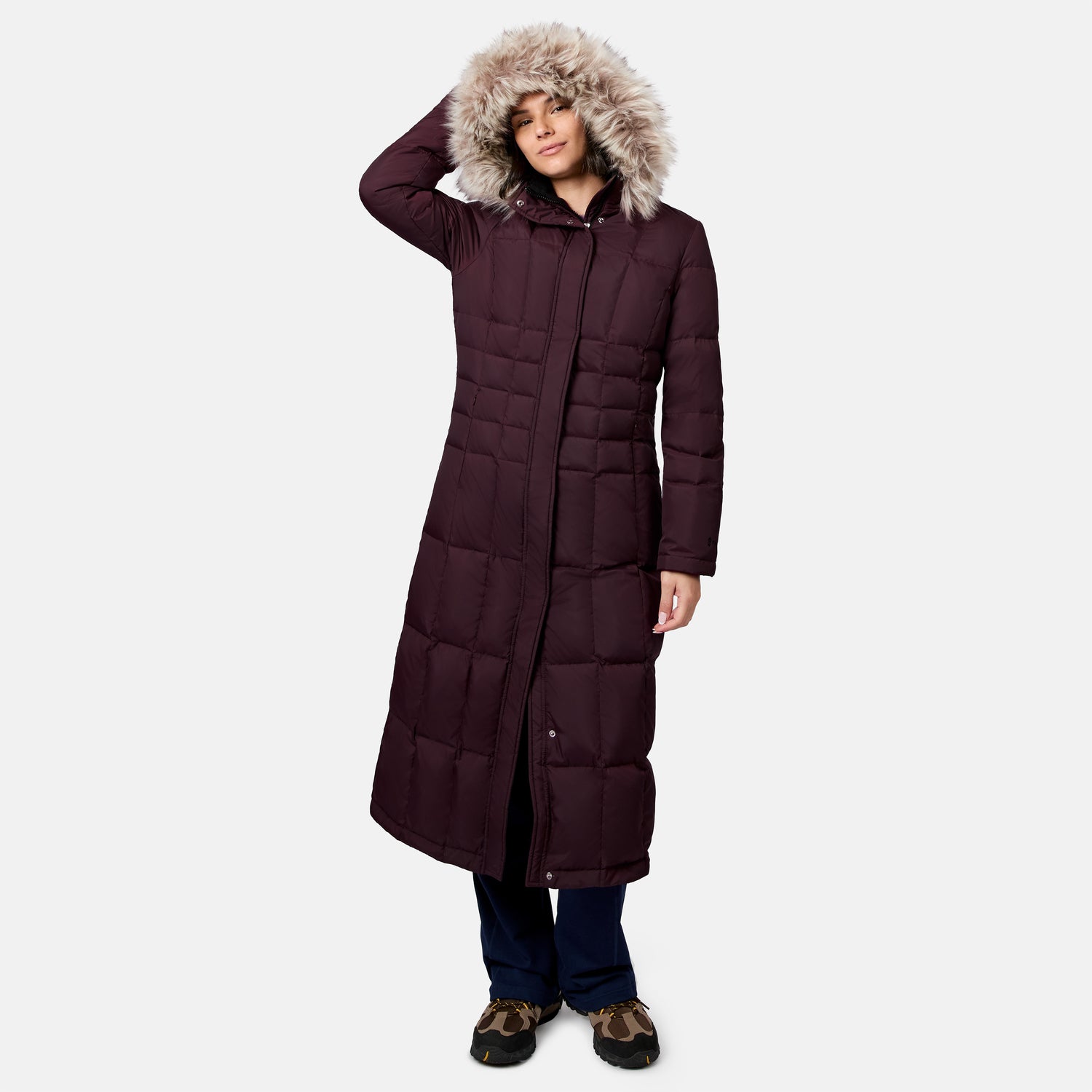 Woman in a burgundy down jacket with fur trimmed hood standing in a studio with navy pants and camo shoes