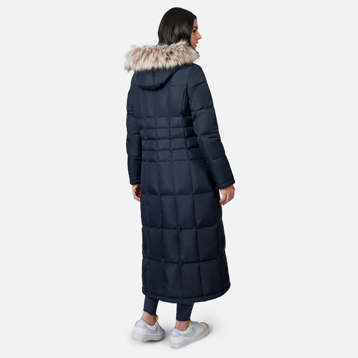 Side view of a model wearing a navy blue full length Splendor down jacket with a fur trimmed hood.