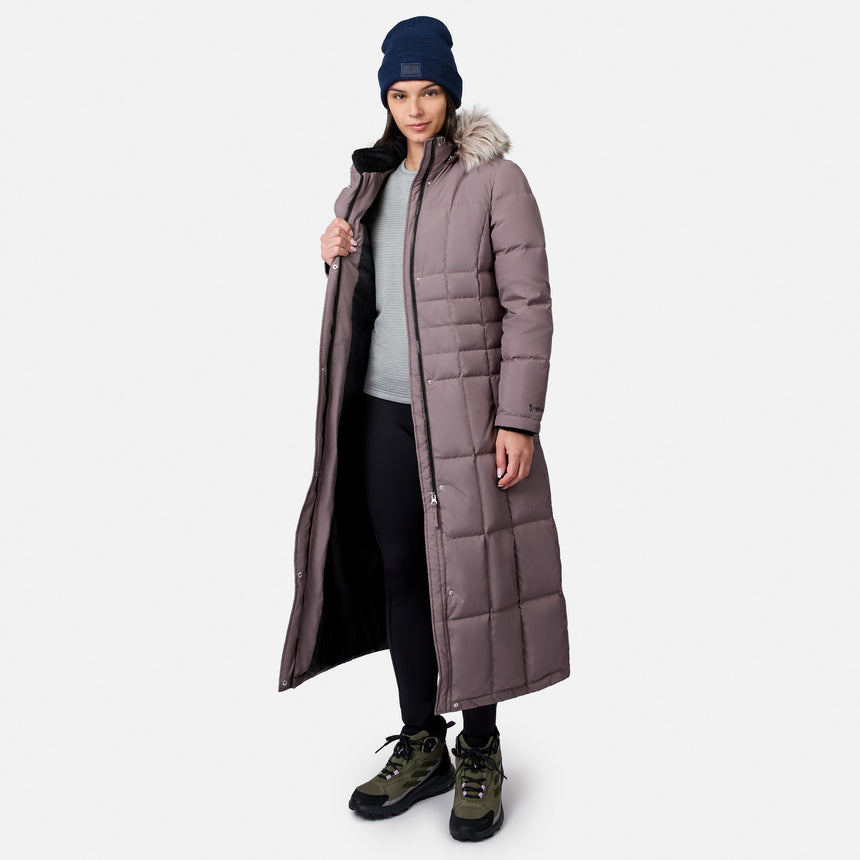 Model wearing a full length mauve Splendor Down Jacket with fur trimmed hood dark blue knit beanie and hiking boots