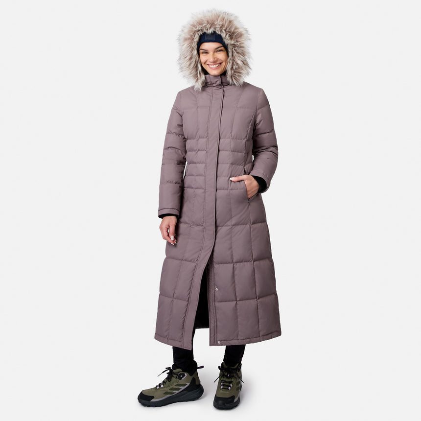 Side view of a woman in a lavender Splendor Down Jacket with a fur hood, hands in pockets, wearing hiking boots.