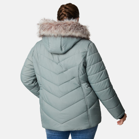 A woman is seen from the back wearing a Free Country Women's Plus Size Unstoppable II Poly Air Touch Jacket in light blue-green with quilted design, faux fur-trimmed hood, and REPREVE fill, standing against a plain white background.