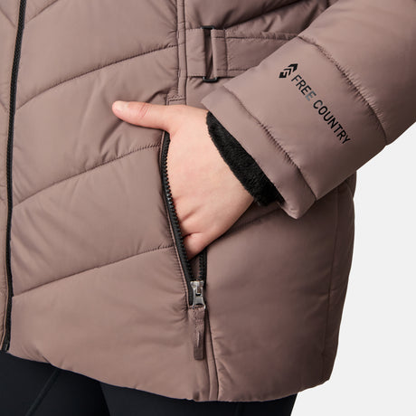 A woman wears the Free Country Women's Plus Size Unstoppable II Poly Air Touch Jacket in taupe, with her hand in the zippered pocket. The eco-friendly jacket has a soft black lining and sustainable REPREVE fill for warmth, plus the brand logo on the sleeve.