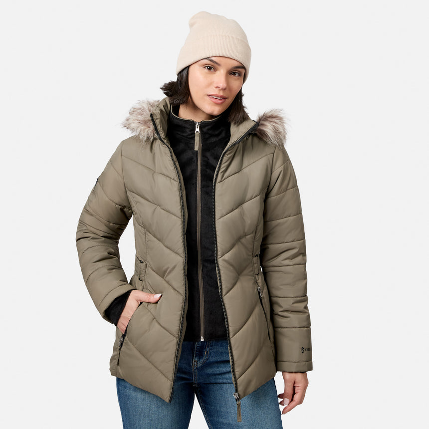 [Model is wearing size S.] A woman wearing an olive green quilted puffer jacket with a faux-fur trimmed hood, a beige knit beanie, a black zip-up top, and blue jeans, photographed against a light gray studio background.