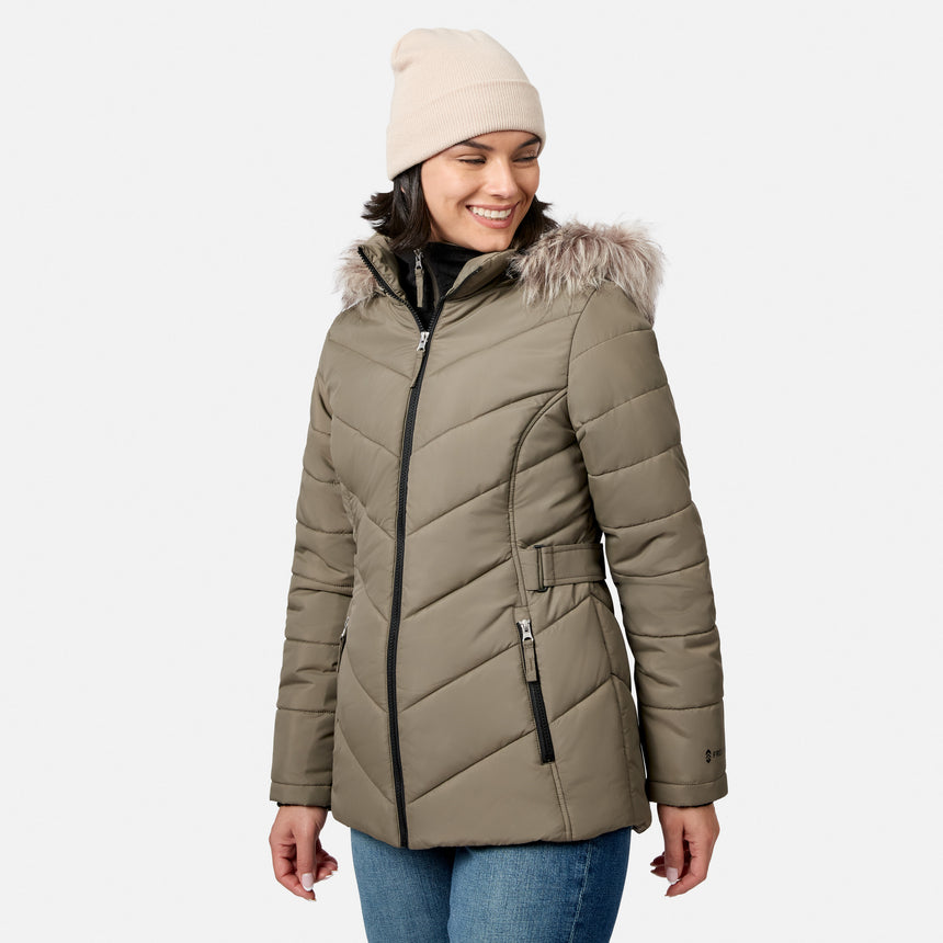 [Model is wearing size S.] A woman wearing a light brown hooded puffer jacket with faux fur trim, a beige knit beanie, and blue jeans, photographed against a light gray studio background.