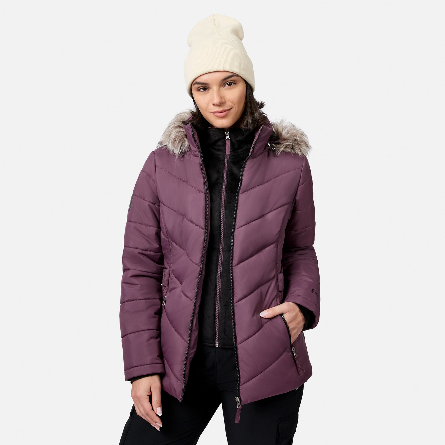 [Model is wearing size S.] A woman wearing a quilted plum purple winter jacket with a faux-fur trimmed hood, a cream knit beanie, and a black zip-up top, photographed against a light gray studio background.