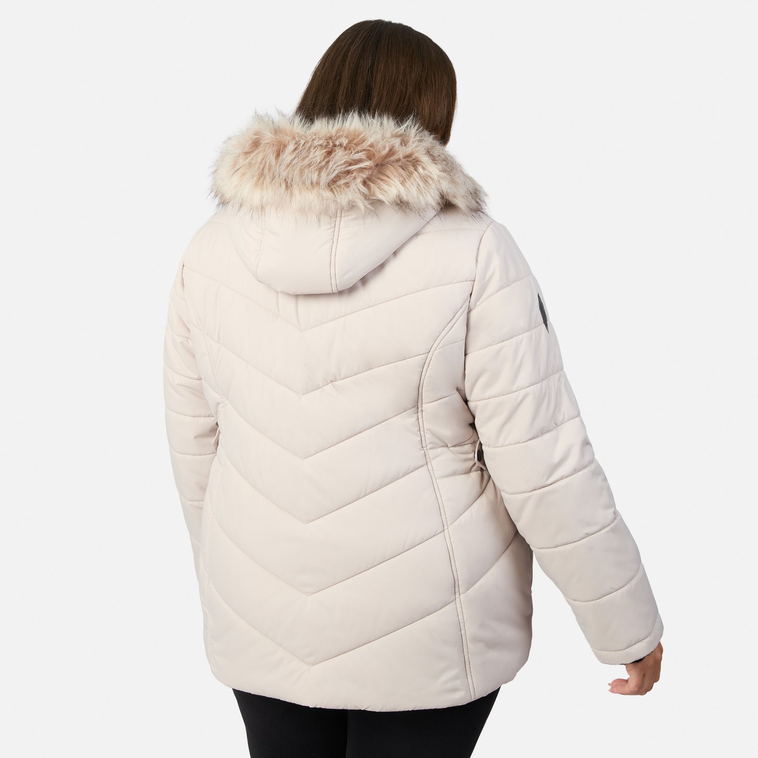[Model is wearing size 1X] A woman viewed from the back wearing a light beige quilted puffer jacket with a fluffy faux-fur trimmed hood, set against a plain light gray studio background.