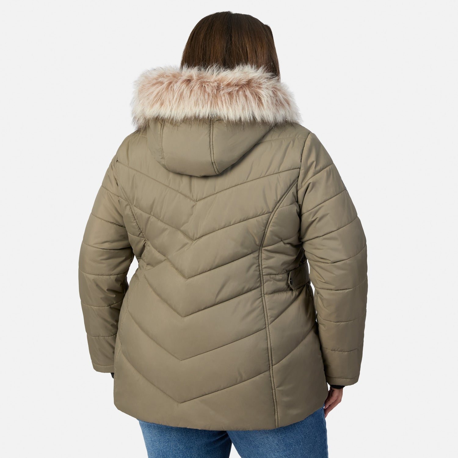[Model is wearing size 1X] A woman viewed from the back wearing a quilted puffer jacket in taupe with a light beige faux-fur trimmed hood, paired with blue jeans, against a light gray studio background.