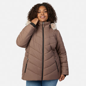 [Model is wearing size 1X] A woman wearing a taupe-brown quilted puffer jacket with a light beige faux-fur trimmed hood and black zippers, paired with blue jeans, against a light gray studio background.