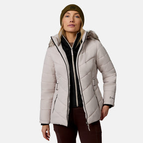 [Model is wearing size S.] A woman wearing a light beige hooded puffer jacket with a faux-fur trimmed hood, a black zip-up fleece layer, brown pants, and an olive green beanie, photographed against a light gray studio background.