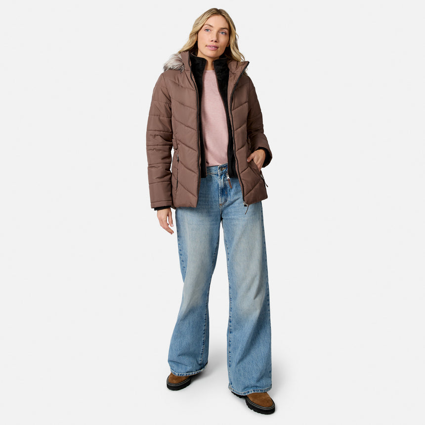 [Model is wearing size S.] A woman modeling a brown puffer jacket with a faux-fur trimmed hood, worn over a pink top and blue jeans, against a plain light gray studio background.