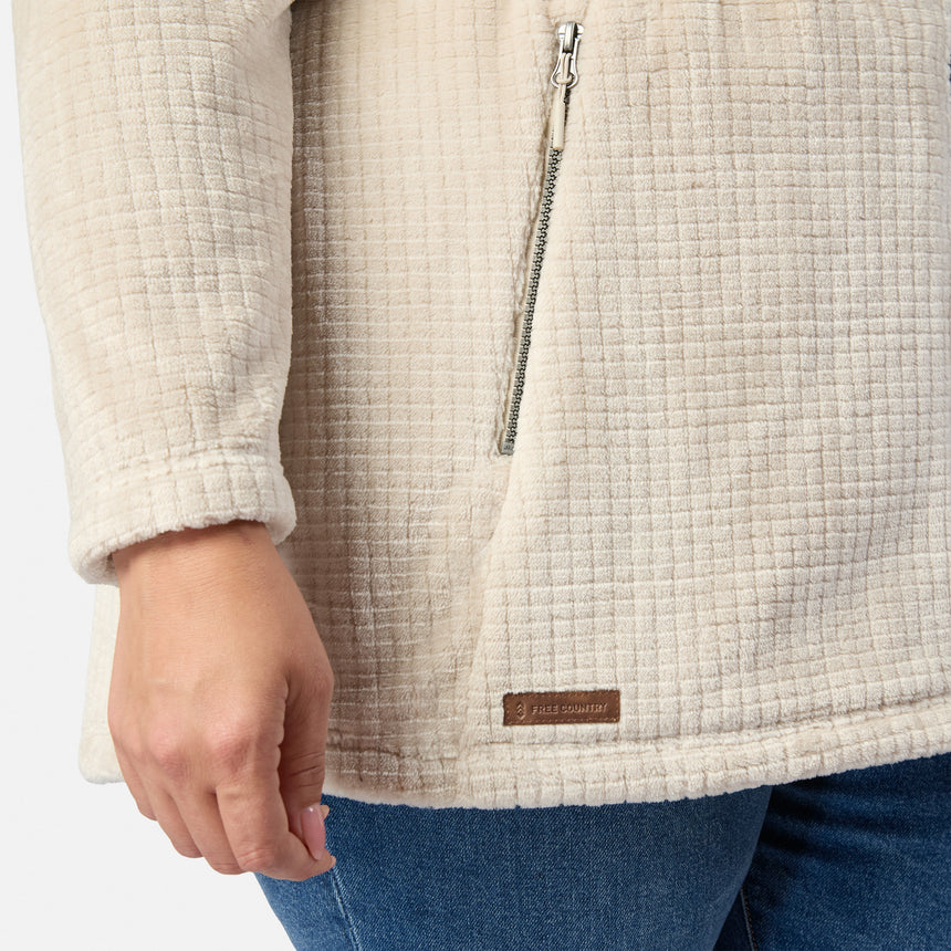 A person wears the cream Free Country Women’s Plus Size Grid Butter Pile® Anorak Jacket, focusing on the lower arm, hand, and side with a small brown label by the hem, paired with blue jeans.