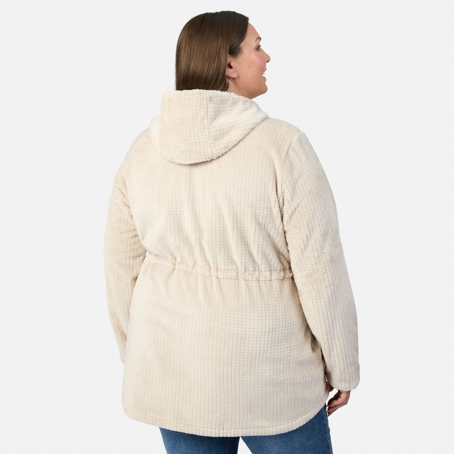 A woman models the Free Country Women’s Plus Size Grid Butter Pile® Anorak Jacket in light beige with blue jeans, standing with her back to the camera against a white background, highlighting its cozy fleece style.