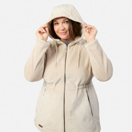 A woman wears the Free Country Women’s Plus Size Grid Butter Pile® Anorak Jacket in light beige, holding the hood with both hands and smiling against a plain light gray background.