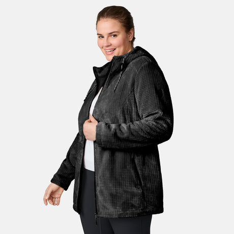 A woman wears a Free Country Women’s Plus Size Grid Butter Pile® Anorak Jacket with hood, standing against a light background, smiling and looking toward the camera.