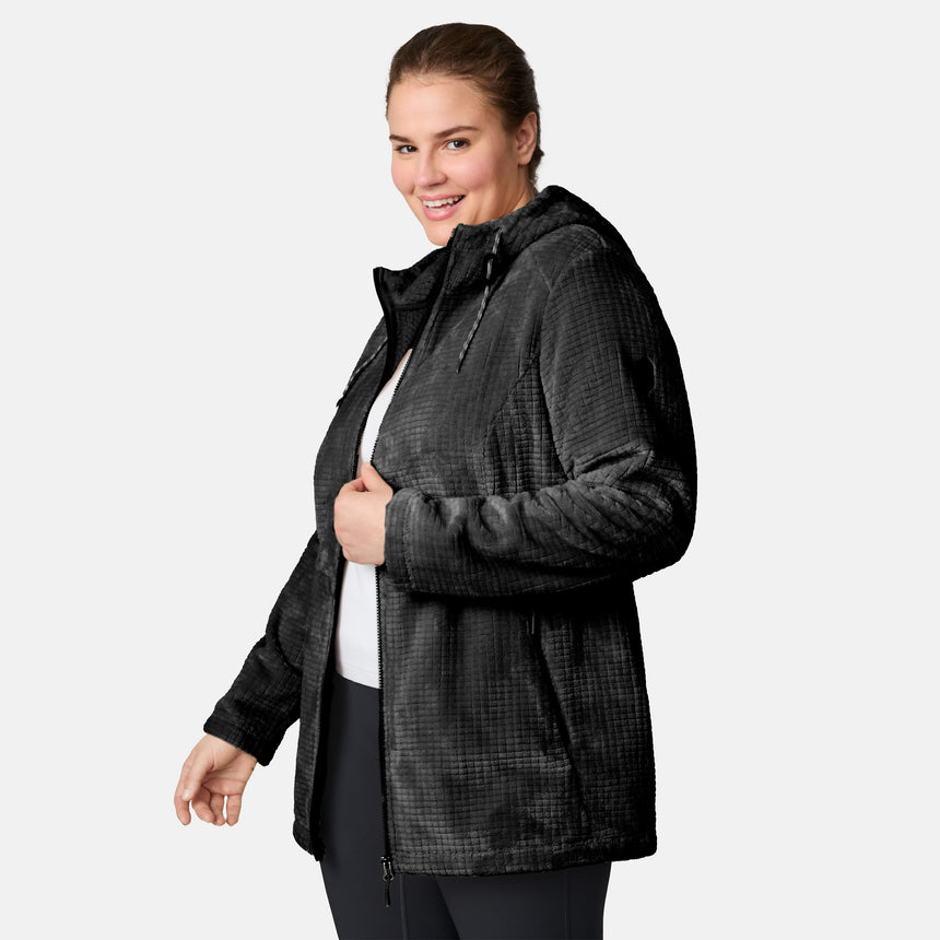 A woman wears a Free Country Women’s Plus Size Grid Butter Pile® Anorak Jacket with hood, standing against a light background, smiling and looking toward the camera.