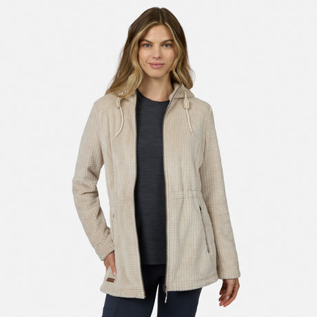A woman models the Free Country Women’s Grid Butter Pile® Anorak Jacket in light beige, hooded with drawstrings, over a dark shirt and pants, standing with one hand in her pocket against a plain white background.
