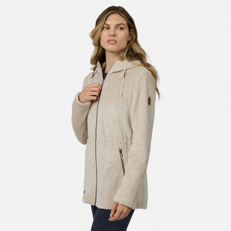 A woman models a light beige Free Country Women’s Grid Butter Pile® Anorak Jacket with zip front, drawstring waist, and hood against a white background, glancing aside while holding the lapel.