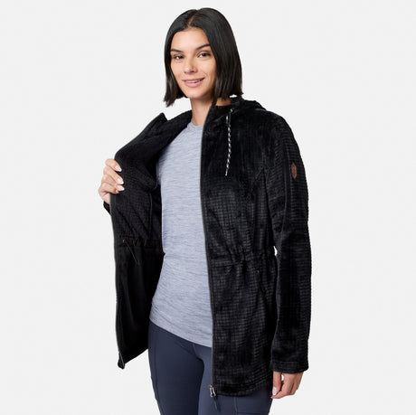 A person wearing a gray shirt and navy pants smiles at the camera against a plain white background while opening the long, black, textured Free Country Women’s Grid Butter Pile® Anorak Jacket to reveal its soft interior.