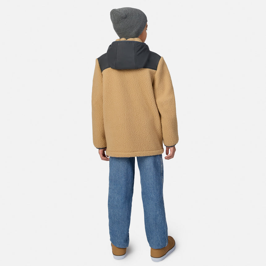 A child shown from the back wearing a tan fleece jacket with a dark gray hood, blue jeans, and brown shoes against a light gray studio background.