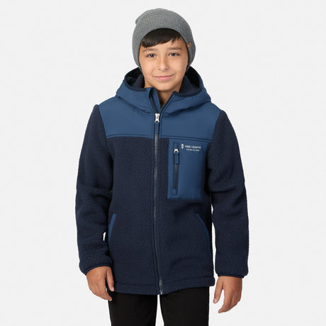 A child wearing a navy and blue fleece zip-up jacket with a hood, paired with a gray beanie, standing against a light gray background.