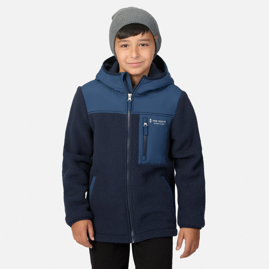 A child wearing a navy and blue fleece zip-up jacket with a hood, paired with a gray beanie, standing against a light gray background.