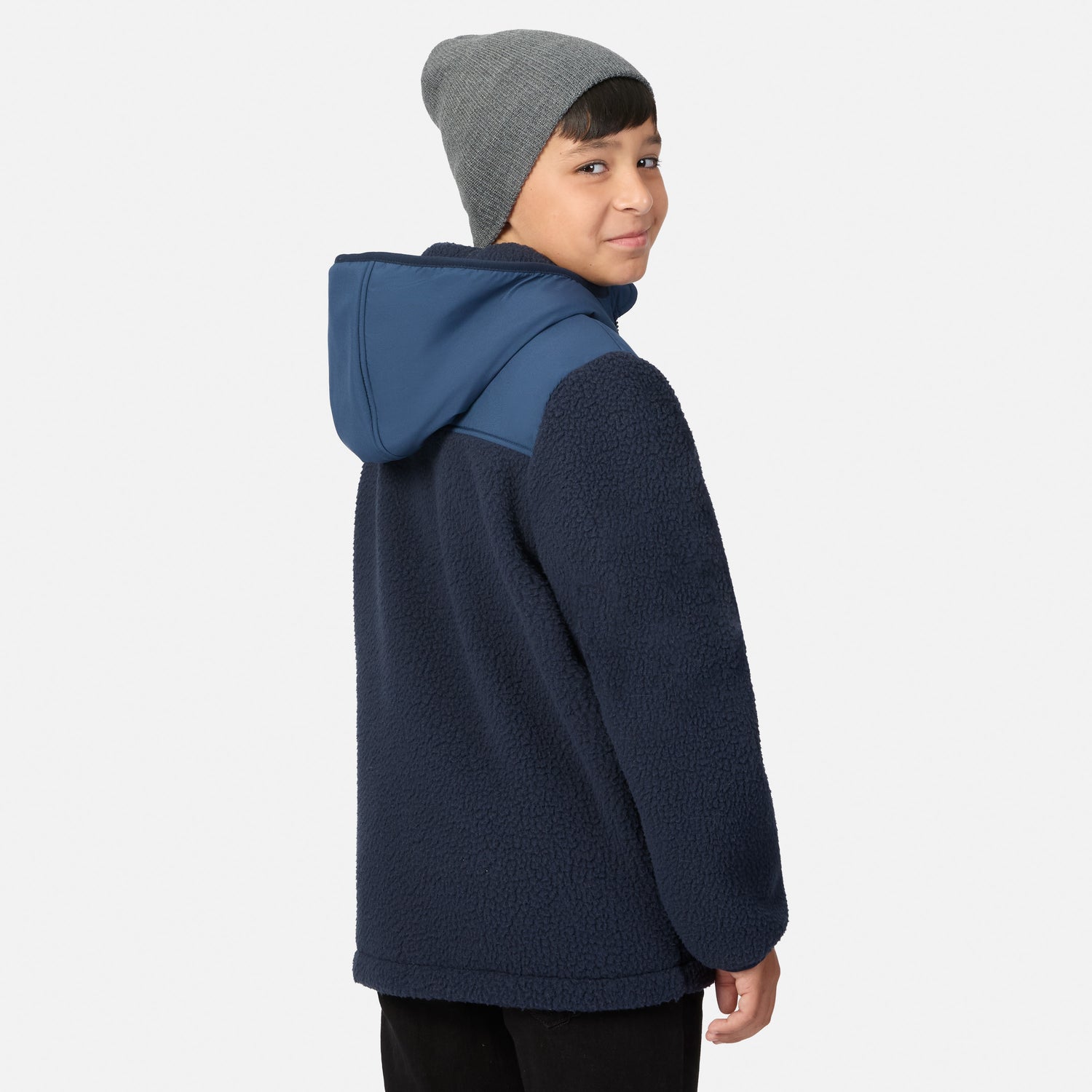 A child wearing a navy blue fleece hooded jacket with a contrasting blue shoulder panel and a gray beanie, shown from a side-back angle against a light gray studio background.