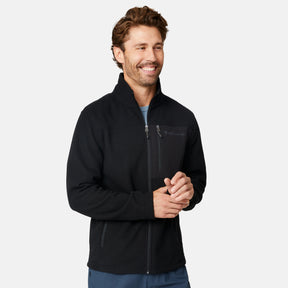 [Matt is 6'2" wearing size M.] Man wearing Free Country Men's Calabaza II Brick Fleece Jacket in Black with a zipper chest pocket, convertible collar, smiling looking forward, light grey background.