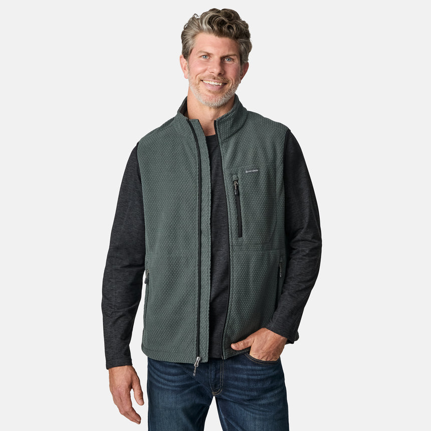 [Kolby is 6'2" wearing size M.] Men’s Free Country green zip-front vest with textured brick pattern and zippered chest pocket—layered over a dark grey long-sleeve shirt and blue jeans. Styled for a laid-back, outdoor-ready look against a clean white background.