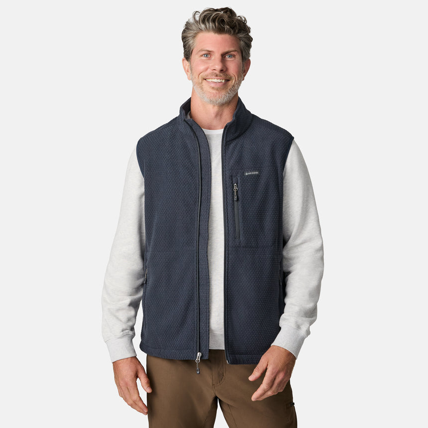 [Kolby is 6'2" wearing size M.] Men’s Free Country navy quilted vest with zippered chest pocket and textured finish—layered over a light gray long-sleeve shirt and brown pants. 