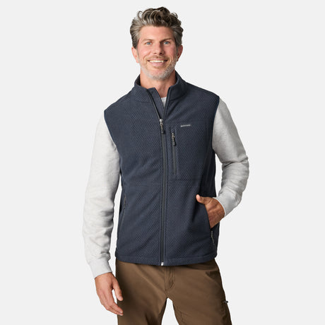 [Kolby is 6'2" wearing size M.] Men’s Free Country navy quilted vest with zippered chest pocket and textured finish—layered over a light gray long-sleeve shirt and brown pants. 