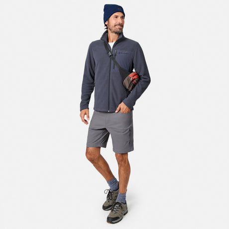 A man in a navy beanie, gray shorts, hiking shoes, and Men’s Calabaza II Brick Fleece Jacket by Free Country stands with a crossbody bag and red flannel shirt tucked in for comfort and layering, posed against a plain white background.