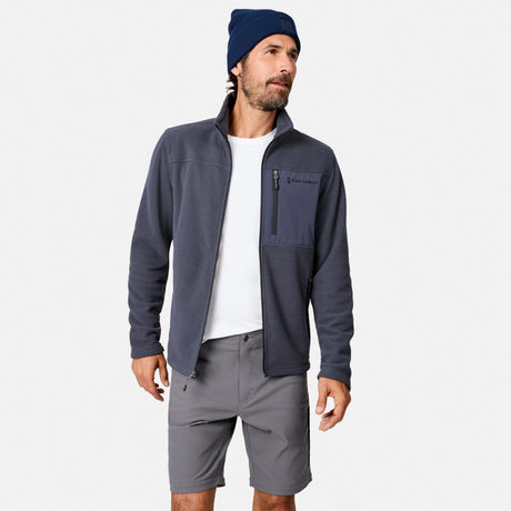 A man in a navy beanie, white tee, and gray shorts stands against a white background, wearing the Free Country Men’s Calabaza II Brick Fleece Jacket—a versatile gray layering piece with chest pocket for superior comfort.
